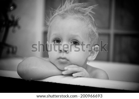 Little boy aged 2 in taking a bath in a old bath top. Only head and arms are visible. Black and white indoor photo. Scandinavian looking. Nordic looking.