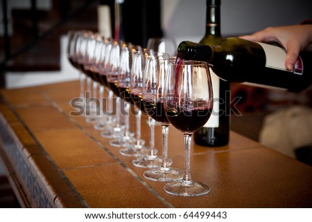 Woman hand with wine bottle pouring a row of glasses for tasting