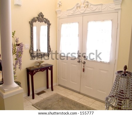 Ornate Entry Hall with white windowed doors, columns,  mirror, key table, tile floor and rug.