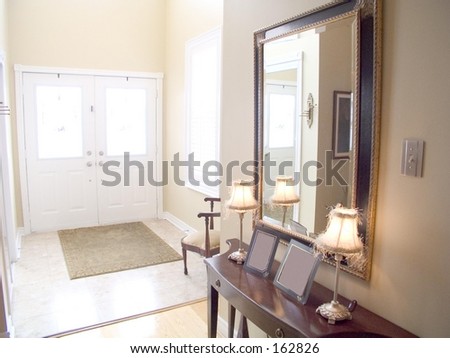 Entry Hall of a house with white doors, windows, chair, lamps, mirror,  table, tile floor and rug.