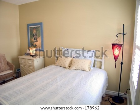 Bedroom with wood floor, white ceiling, window, red lamp, bedside table and throw pillows
