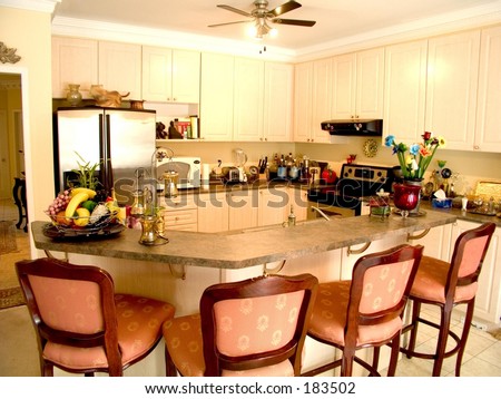 Modern kitchen with island table, four chairs, fridge, stove and ceiling fan.