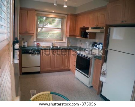 Modern kitchen with cabinets, chair, fridge, dishwasher, stove, ceiling lights and two windows.