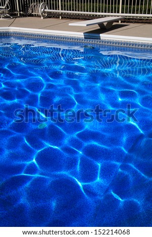 A Diving Board And Deep Blue Swimming Pool Water Forming Abstract Patterns Created By Sunlight Dancing On The Undulating Surface