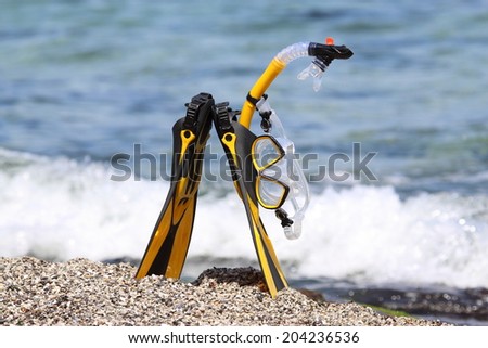 Flippers, mask and snorkel lying on sandy beach. Sea waves background.