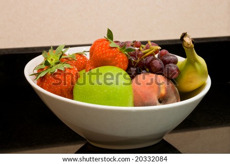 Close up of white fruit bowl with apple, strawberries, peach, banana and grapes