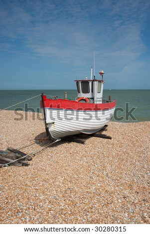 Red and white fishing boat on shingle beach with sea and blue sky in the background