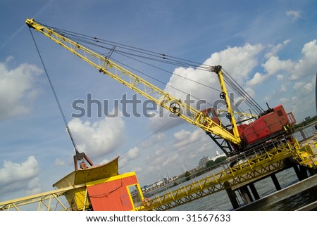 Yellow and red crane by the river against blue sky with white clouds, London, UK