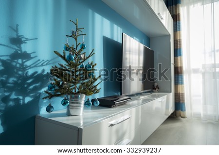 small decorated Christmas tree in a bucket on the furniture in the living room in a pleasant interior, tuned in the colors turquoise