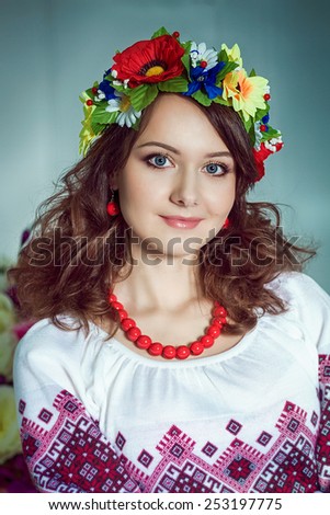 Closeup portrait of beautiful girl with red necklace and flowers wreath . Red earrings .Ukrainian national clothes.
