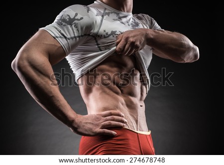 Muscular young man in studio on dark background shows the different movements and body parts