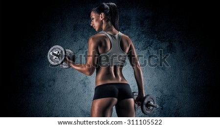 Muscular young woman in studio on dark background shows the different movements and body parts