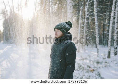 A hipster man standing alone in the winter snowy forest