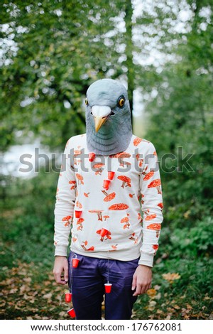 hipster young man in a creepy pigeon mask in the forest