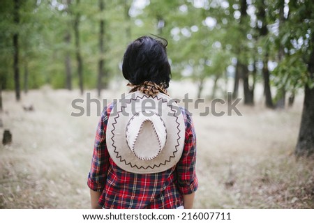 cowgirl standing with her back to the camera in the forest