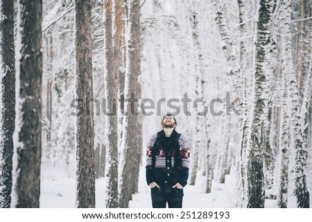 Young hipster man looking up at the sky in the winter snowy forest