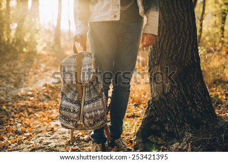 Hipster man standing by the sunset forest tree holding in his hands his backpack