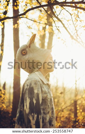 man half took off his rubber bird mask, standing in the autumn sunset forest thinking dramatically