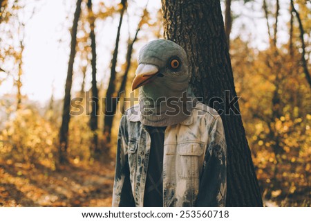 Weird man in a creepy rubber pigeon bird mask in the autumn sunset forest