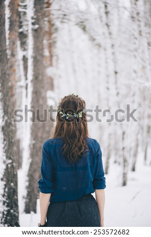 Beautiful brunette standing in the snowy winter forest wearing a cute head band, standing back to the camera