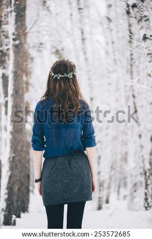 Beautiful brunette standing in the snowy winter forest wearing a cute head band, standing back to the camera