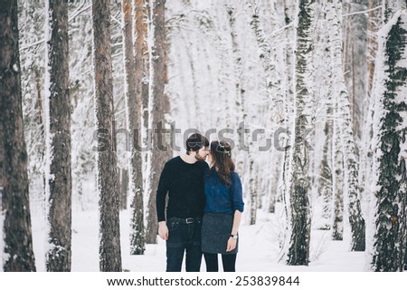 Young happy couple kissing and hugging, looking each other in the eyes in the winter snowy forest