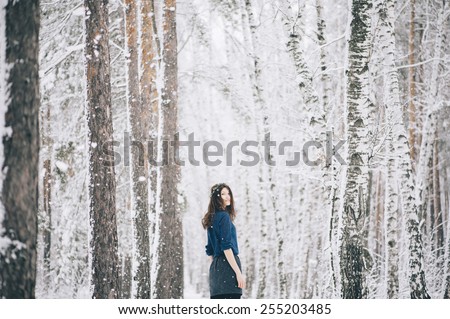 Beautiful brunette woman wearing a wreath turning back to the camera in the winter snowy forest