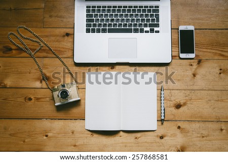 Laptop keyboard, pen, touchscreen smartphone, film camera and a book on a wooden table background