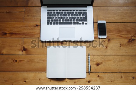 Business laptop, touch screen smartphone, paper notebook and a pen on the old wooden table background