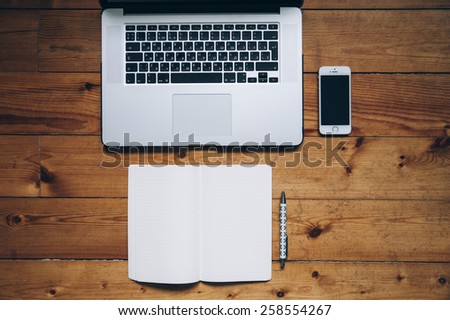 Business laptop, touch screen smartphone, paper notebook and a pen on the old wooden table background