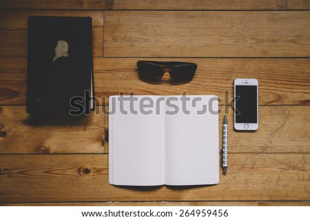 Paper notebook, black old book, sunglasses, pen and a touchscreen smartphone on the old wooden table background