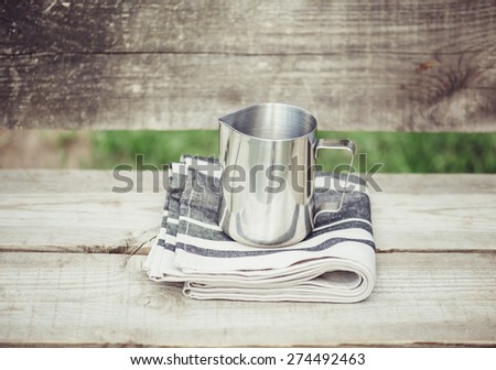 Frothing milk pitcher on the cloth napkin on the wooden background