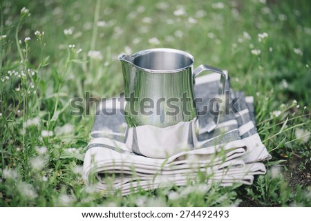 Frothing milk pitcher on the cloth napkin outdoors on the green grass background