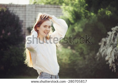 Young red head woman happily laughing outdoor, touching her long red hair.