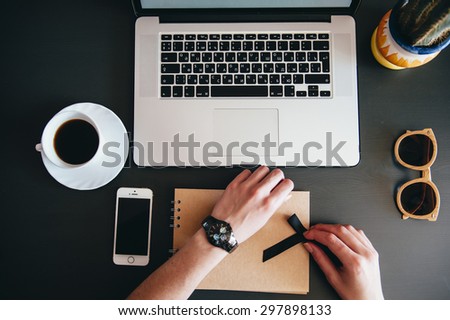 Woman working at the office table. Top view of human hands, laptop keyboard, coffee,smartphone,sunglasses,notebook and a cacti on a wooden table background
