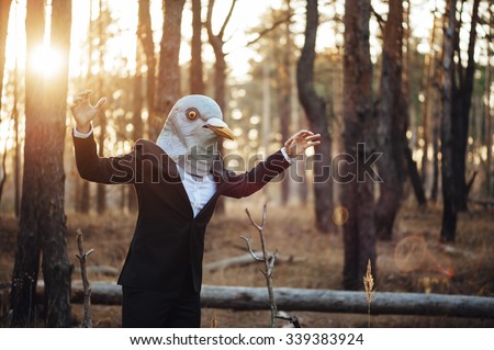 Weird businessman in a rubber bird mask pretending to fly in the sunset forest