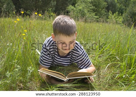 Boy 10 years old reading a book lying on the grass