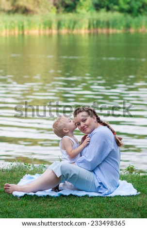 Pregnant woman and her son 2 yo on the green grass. Concept of motherhood and femininity