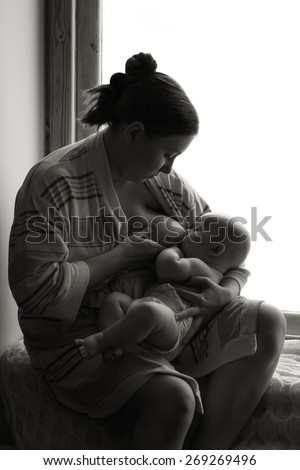 Woman breastfeeding near a window, baby napping, black and white