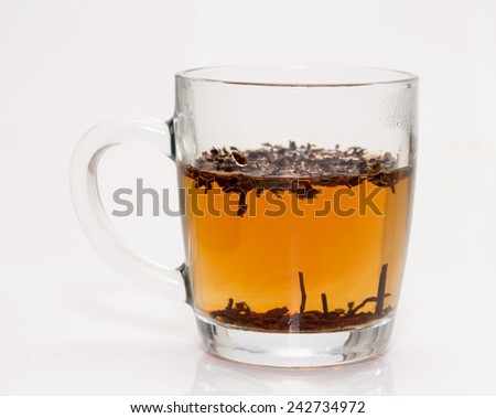 A transparent glass filled with brown leaves and yellow liquid.