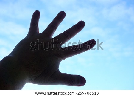 Silhouette of human hand on sky background