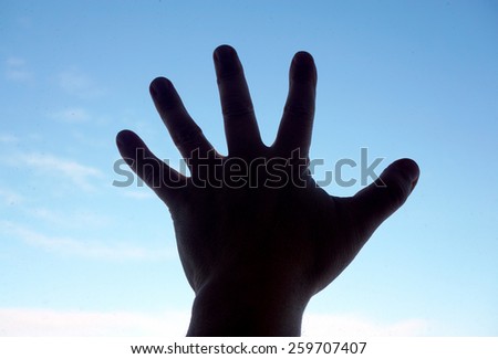 Silhouette of human hand on sky background