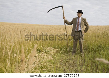 man in suit and hat with scythe standing in field with golden grass