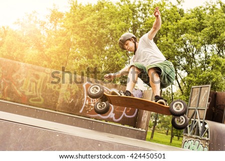 Skateboarder doing a jumping trick at skateboard park with mountain board. Lens flare effect.