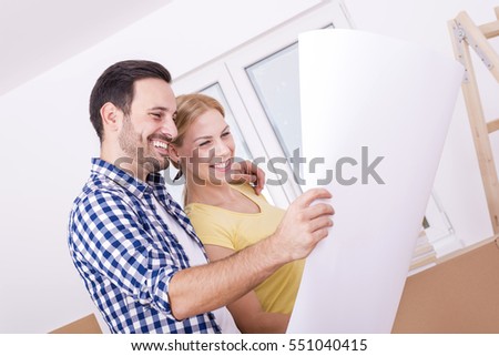 Young smiling couple discussing plan of their new house while holding paper drawing.