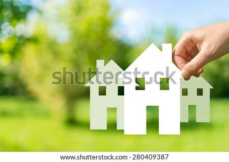 Hand holding cut off white paper house in nature as symbol of mortgage