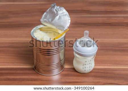 Powdered milk formula in can and bottle for feeding baby on wooden table.