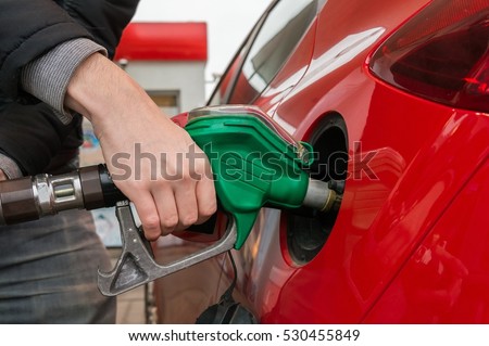Man is pumping gas in red car in fuel station.