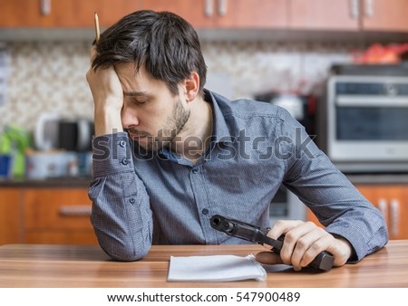 Depressed man is writing letter and holds pistol in hand. Suicide concept.