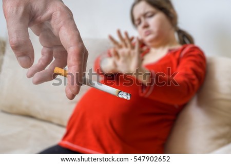 Passive smoking concept. Selfish man is smoking cigarette near pregnant woman.